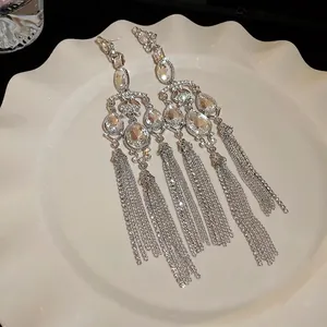Elegant silver needle earrings with teardrop crystals and long tassels on a white plate.