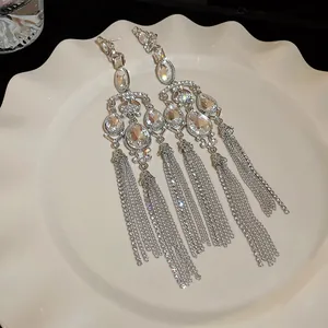 Macro view of crystal water-drop tassel earrings on a white decorative plate.