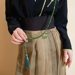 Detailansicht einer langen grünen Perlenkette mit blauer Quaste auf Kleidung im China-Stil
