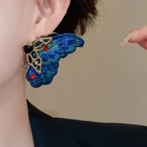 Dettaglio dell'orecchino a farfalla ricamato blu con strass e cuore dorato lucido