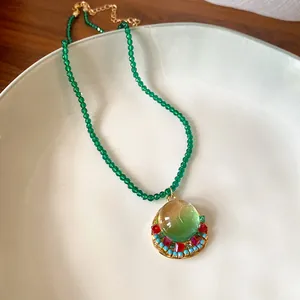 Close-up of vintage French style green beaded necklace with gradient resin pendant.