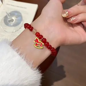 Detailed view of a red agate beaded bracelet with a gold rocking horse charm on a wrist