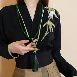 Detail einer grünen Perlenkette mit ethnischer Quaste an einem chinesischen Oberteil