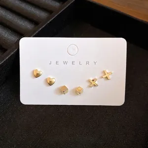 Set di orecchini a lobo dorati minimalisti con forme a cuore e cubo su cartoncino
