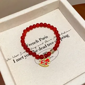 Detailed macro view of a red agate beaded bracelet with a gold rocking horse charm in a box