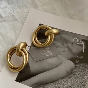 Detailaufnahme von mattgoldenen geometrisch verschlungenen Creolen im Retro-Stil