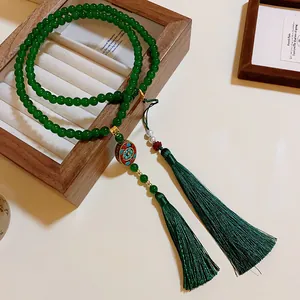 Detailansicht einer grünen Perlenkette mit doppelten Quasten und Emaille-Anhänger.