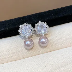 Close-up detail of elegant zircon flower earrings with pink pearl drops on beige fabric