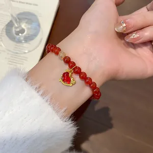 Close-up of a red agate beaded bracelet with a gold rocking horse charm on a woman's wrist.