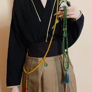 Detail von grünen und gelben Perlenketten auf traditioneller chinesischer Kleidung.