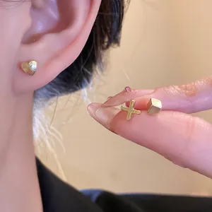 Primo piano di un set di orecchini d'oro minimalisti con cuore, croce e cubetto per le donne