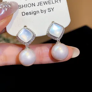 Close-up of elegant zircon and pearl drop earrings with a mother-of-pearl stud detail.
