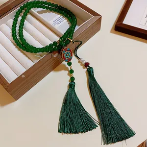 Nahaufnahme einer grünen Perlenkette mit Quasten und Emaille-Anhänger