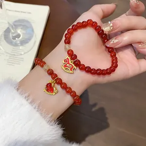 Close-up of red agate beaded bracelet with golden rocking horse charms on wrist.