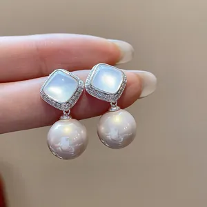 Close-up of elegant silver stud earrings featuring square zircons and large pearl drops