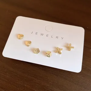 Dettaglio di set di orecchini a perno dorati minimalisti con forme a cuore, cubo e croce