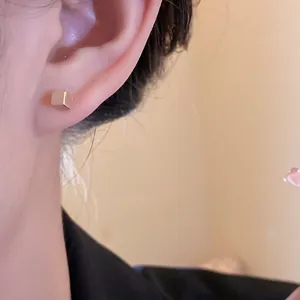 Dettaglio di un orecchino a perno a cubo dorato minimalista indossato sull'orecchio, stile chic
