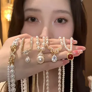 Close-up of multiple gold-plated pearl necklaces with CZ pendants held by hand.