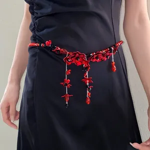 Close-up detail of a red glass flower beaded waist chain with tassels on a black dress