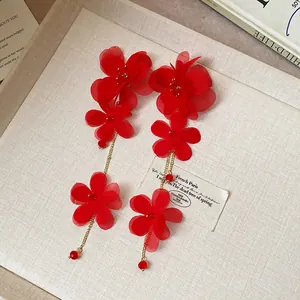 Detailed macro view of elegant red chiffon flower tassel drop earrings on a textured tray