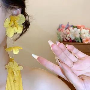 Detailed close-up of elegant yellow chiffon flower tassel earrings worn by a female model