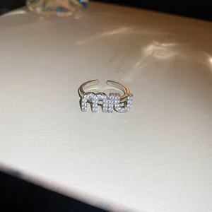 Vue rapprochée d'une bague ouverte argentée ornée d'un lettrage miu scintillant de cristaux