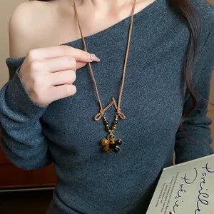 Close-up detail of a tiger's eye flower pendant necklace worn over a grey sweater
