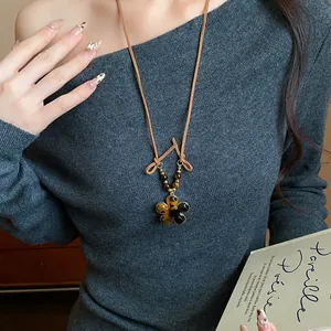 Close-up of a Maillard-style flower necklace with tiger eye stone on a grey sweater.