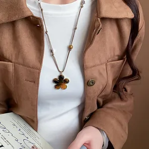 Detailed view of a brown tiger eye flower necklace styled with a Maillard jacket