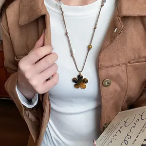 Close-up of Maillard tiger eye flower pendant necklace on model wearing suede jacket