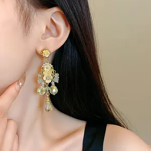 Close-up detail of ornate floral tassel earrings with green crystal teardrops.