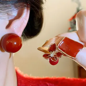 Detail view of stylish deep red resin ear studs in ball, flower, and geometric designs