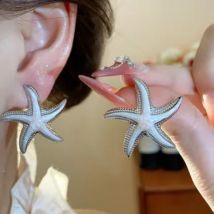 Detail showing starfish stud earrings with white enamel inlay worn on ear and held.