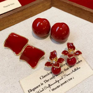 Detail view of red resin stud and flower earrings on a textured wooden tray