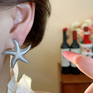 Detailed close-up of a pearlescent white starfish stud earring worn on a model's ear.