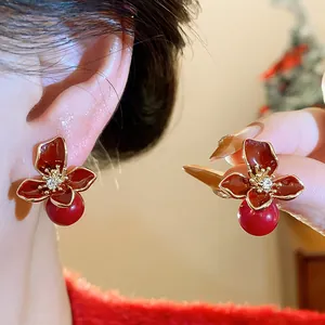 Close-up of red flower stud earrings with a pearl drop and sparkling rhinestone center.