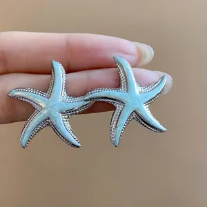 Macro view of mint blue oil-dripped starfish stud earrings with silver textured borders