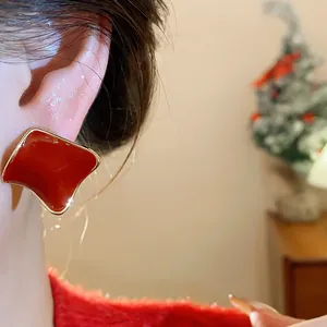 Macro detail of elegant red resin square stud earring with gold-tone border worn on ear