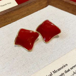 Close-up view of minimalist deep red resin stud earrings featuring elegant gold border details