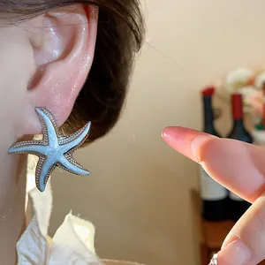 Close-up of a stylish silver starfish stud earring with blue enamel on a person's ear.
