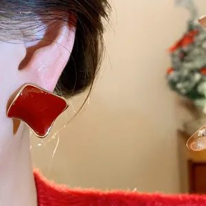 Close-up view of an elegant red resin square stud earring with gold trim on a model ear
