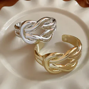 Detail shot of wide gold and silver knotted cuff bracelets on a wavy ceramic plate.