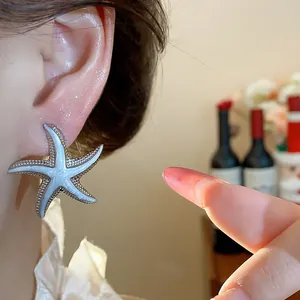 Close-up of silver-tone starfish stud earring with white enamel center worn on the ear