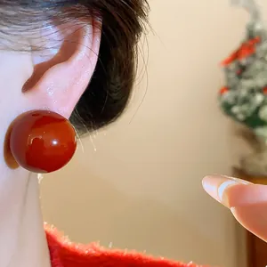 Detailed close-up showing a glossy Ankora red resin sphere stud earring on a model's ear.