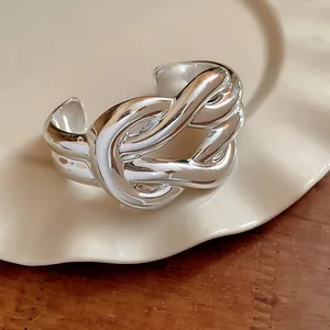 Detail view of a chunky silver knotted cuff bracelet on a vintage cream plate