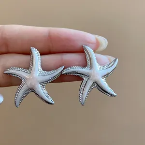 Detailed macro view of silver-tone starfish stud earrings with elegant white enamel finish.