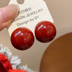 Close-up of glossy Ancola red resin spherical stud earrings with silver needles