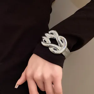 Macro detail view of a chunky silver cross knot bracelet styled over a chic black sleeve