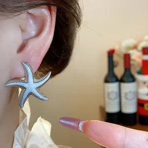 Close-up view of a silver starfish earring with white enamel details worn on an ear.
