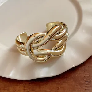 Close-up of a chunky gold-toned knot cuff bracelet with a polished metallic finish